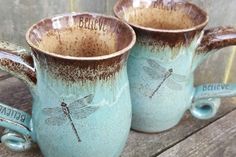 two blue mugs with dragonflies on them sitting on a wooden table next to each other