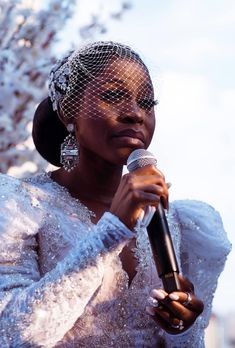 a woman in a white dress holding a microphone and wearing a birdcage veil