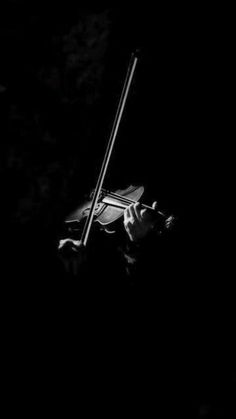 black and white photograph of a person holding a violin in the dark with one hand