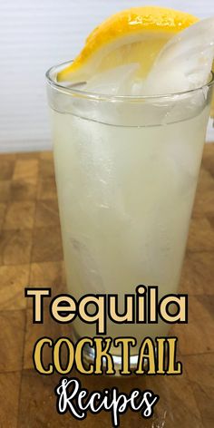 a tall glass filled with ice and lemon wedged into it on top of a wooden table