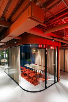 an empty conference room with red chairs and a table in the center is seen through glass walls