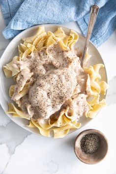 a white plate topped with pasta covered in gravy next to a bowl of seasoning