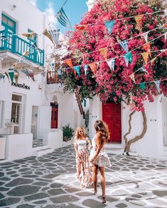 two women walking down the street in front of some buildings with colorful flowers on them