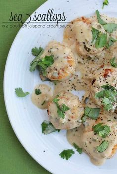 a white plate topped with scallops covered in gravy and garnished with parsley