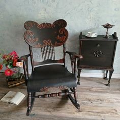 an old fashioned rocking chair next to a table with flowers on it and a book