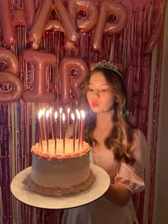 a woman holding a cake with lit candles in front of balloons that say happy birthday