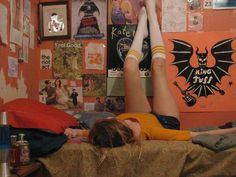 a woman laying on top of a bed next to a wall covered in pictures and posters