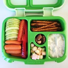 a green lunch box with carrots, apples, celery and other food