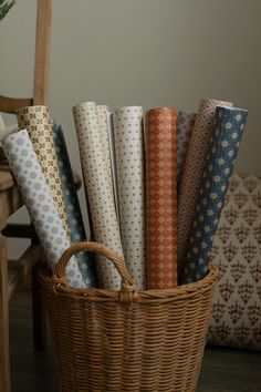 a wicker basket filled with different types of wrapping paper on top of a wooden floor