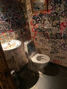 a bathroom with graffiti all over the walls and toilet seat cover in front of it