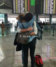 two people hugging each other in an airport with luggage on the ground and signs above them