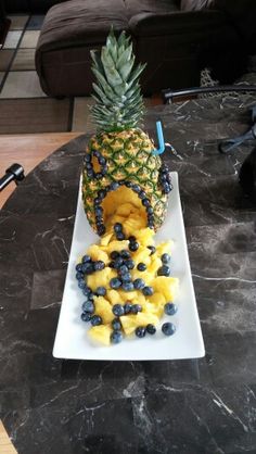 a pineapple with blueberries and bananas on a white plate next to a black table