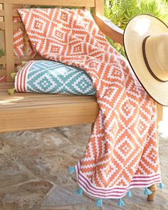 an orange and white blanket sitting on top of a wooden bench next to a hat