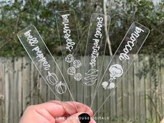 a person holding up four clear plastic wine glasses with words on them and vegetables in the bottom