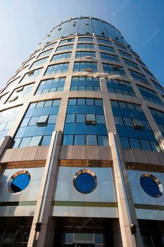 a tall building with round windows and blue sky reflected in it's glass front