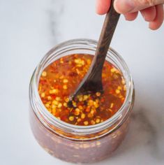 a person holding a spoon in a jar filled with chili paste and corn kernels