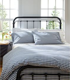 a bed with gingham sheets and pillows in front of two windows, next to a night stand