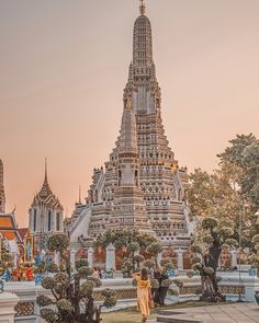 a woman standing in front of a tall building with many spires and trees around it