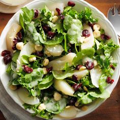 a white bowl filled with lettuce and cranberries on top of a wooden table