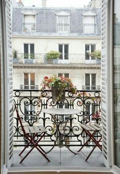 a balcony with chairs, table and potted plant on the window sill in front of an apartment building