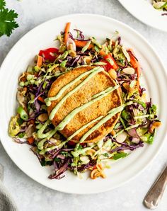 a white plate topped with meat and veggies next to a bowl of salad