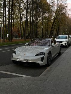 a silver sports car parked on the side of a road next to a tree lined street