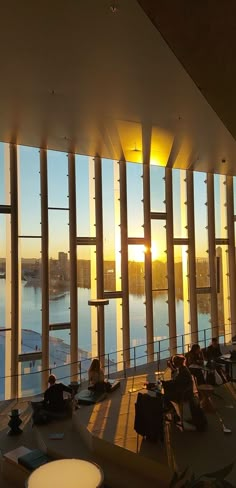 people are sitting on the floor in front of large windows looking out at water and buildings