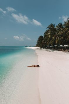 a person laying on the beach in front of some palm trees and clear blue water