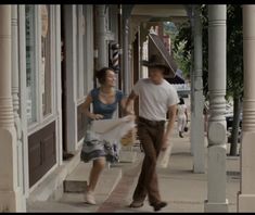 a man and woman walking down the sidewalk in front of storefronts holding shopping bags