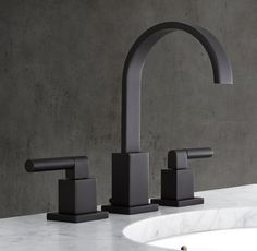 two black faucets sitting on top of a white sink next to a gray wall