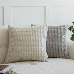 two pillows sitting on top of a white couch next to a potted green plant