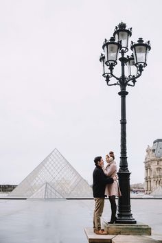 a man and woman standing next to a lamp post in front of the pyramids