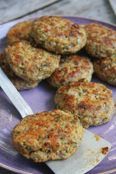 several crab cakes on a purple plate with a fork and knife next to them,