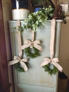 three wreaths tied to the side of an old refrigerator with ribbon and flowers on top