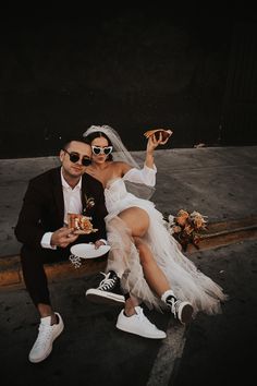 a man and woman sitting on the ground with food in their hands while wearing sunglasses