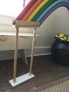 a rainbow sculpture sitting on top of a wooden floor next to a potted plant