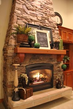 a stone fireplace in a living room with potted plants on the mantle and a clock above it