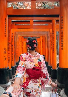 a woman in a kimono walking through an orange - colored tunnel with red flowers on her hair