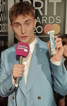 a man in a blue suit is holding a microphone and talking into a pink mic