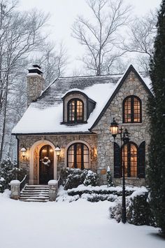 a stone house is covered in snow and lit up by lights on the front door