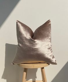 a brown pillow sitting on top of a wooden stool next to a white wall and chair