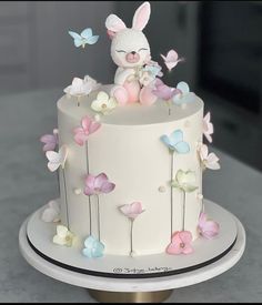 there is a white cake decorated with flowers and a bunny on the top, surrounded by butterflies