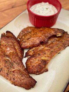 three pieces of meat on a plate with a small bowl of sour cream in the background