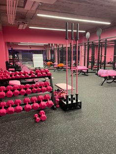 an empty gym with rows of pink dumbs and black racks on the floor in front of them