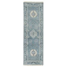 a light blue rug with an ornate design on the bottom and sides, in front of a white background