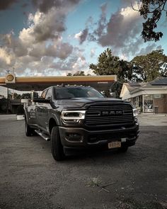 a black ram truck parked in front of a gas station with a sky filled with clouds