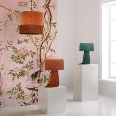 three lamps are sitting on pedestals in front of a wallpapered room with pink flowers