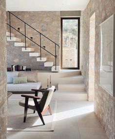 a living room filled with furniture next to a stone wall and stairs that lead up to the second floor