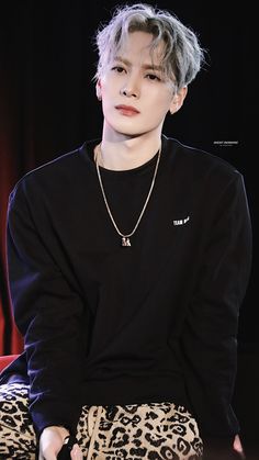 a young man sitting on top of a leopard print chair wearing a black shirt and silver necklace