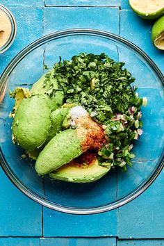 a glass bowl filled with avocado, cilantro and seasoning on top of a blue table